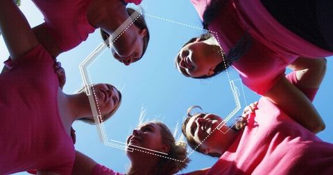 Huddling women in pink t-shirts linking arms under blue sky for teamwork and unity