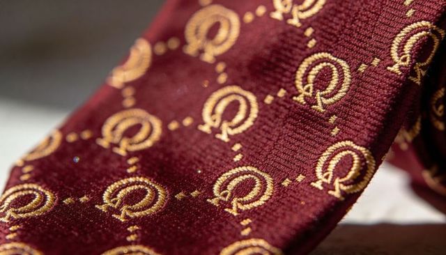 Displaying burgundy silk necktie with gold embroidered motifs and woven texture details
