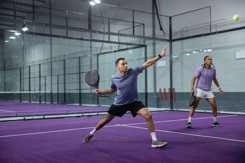 Men playing padel on purple indoor court lunging for shot during competitive doubles rally
