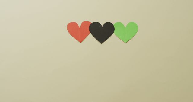 Three colored paper hearts in a row on beige background, creating a minimalistic and symmetrical look. Ideal for concepts related to love, decoration, Valentine's Day, and simple designs. Can be used for greeting cards, social media posts, or decorative purposes.