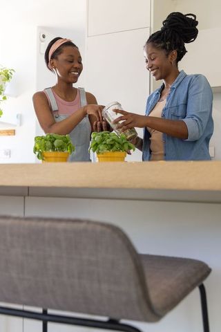 Mother and daughter tending herb pots at bright modern kitchen island, smiling together