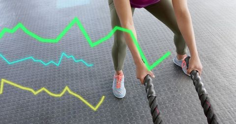 Woman exercising with battle ropes and digital graph overlay