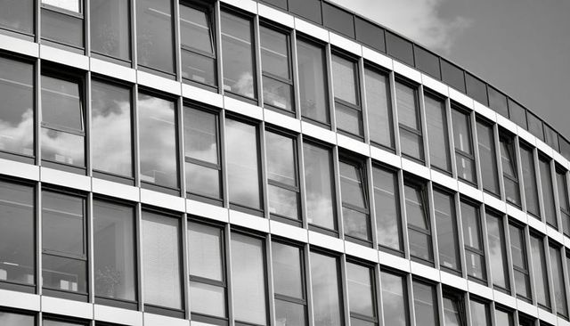 Curved office facade reflecting clouds in monochrome glass curtain wall with metal grid