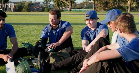 Youth teammates sitting in circle on grass sharing helmets, gear and sports camaraderie