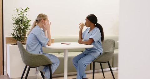 Nurses taking break and sipping coffee in modern breakroom, diverse female medical staff