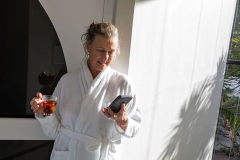 Senior woman relaxing with smartphone and tea in bright environment