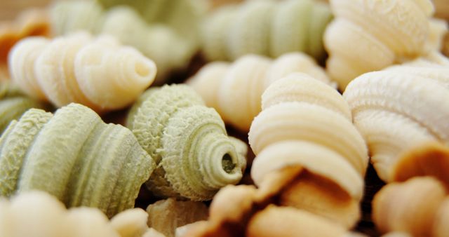 This image shows a close-up of mixed handmade pasta shapes in beige and green tones. Use this image for promoting gourmet food products, illustrating recipe books, food blogs, or for marketing Italian cuisine restaurants. Ideal for emphasizing the artisanal quality and unique textures of the pasta.
