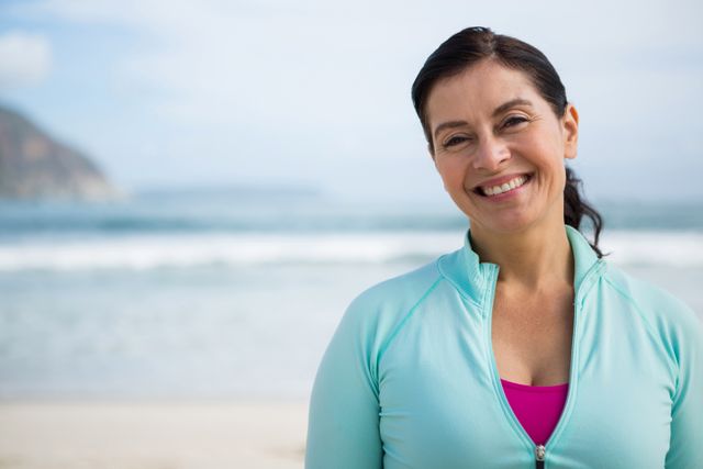 Woman enjoying a winter day at the beach, smiling and looking relaxed. Ideal for use in advertisements promoting outdoor activities, healthy lifestyles, and leisure. Suitable for travel brochures, wellness blogs, and social media content highlighting the benefits of spending time in nature.