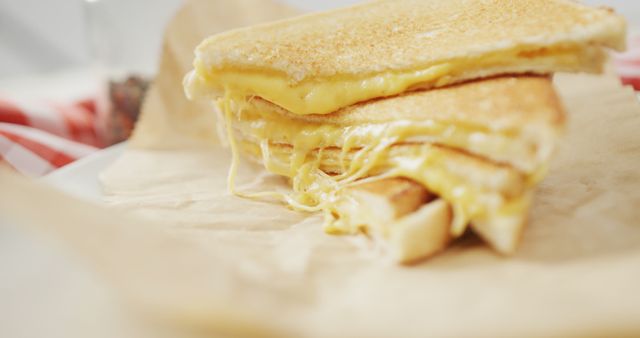This close-up image showcases a perfectly golden and crispy grilled cheese sandwich with melted cheese oozing from between two layers of toasted bread, placed on Kraft paper. Ideal for use in food blogs, menus, recipe books, and advertisements promoting comfort food or lunchtime snacks.