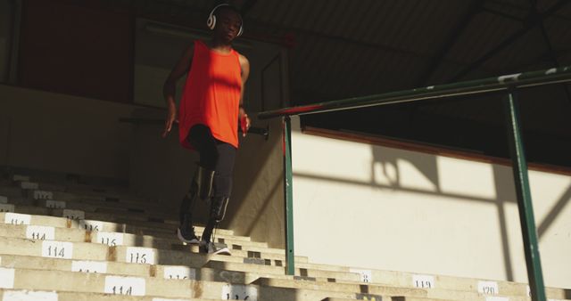 African american male athlete with prosthetic legs in headphones tarining on steps of stadium. Sport, athletics, training and fitness, unaltered.