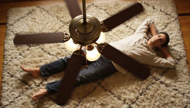 Man lying relaxed on plush shag rug under spinning brass ceiling fan, cozy home moment