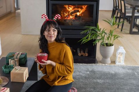 Woman Enjoying Warm Beverage by Fireplace with Christmas Gifts