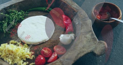Rustic wooden serving board with dough disc, cherry tomatoes, garlic and chili, herbs & sauce cup