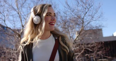 Young woman listening to music with headphones while walking through urban sunlight