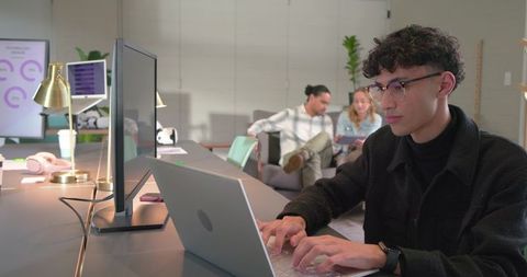 Young professional working on laptop in modern coworking space with team collaborating