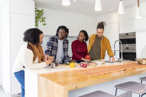 Diverse group chopping veggies and chatting at bright kitchen island prepping meal