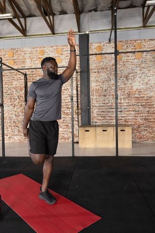 African american athlete performing standing quad stretch on red mat in industrial gym
