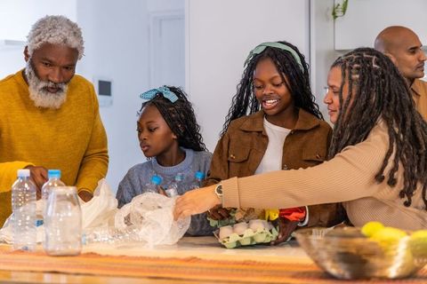 Multi-generational black family gathering and sorting recyclables at bright kitchen counter