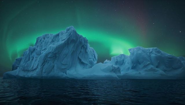 Emerald aurora borealis lighting massive iceberg over calm polar ocean night panorama