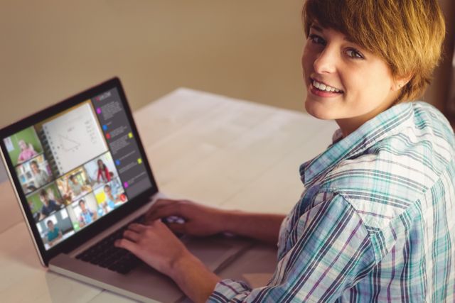 Young woman participating in an online video conference, smiling to the camera while typing on a laptop. Ideal for illustrating remote work, digital communication, virtual learning, and the work-from-home lifestyle.