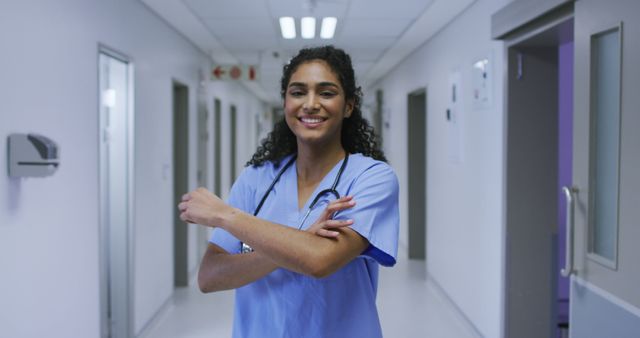 Nurse standing confidently in hospital corridor, dressed in scrubs and holding a stethoscope. Ideal for use in medical and healthcare-related content, including hospital marketing materials, medical journals, and healthcare websites promoting nurse and staff recognition.