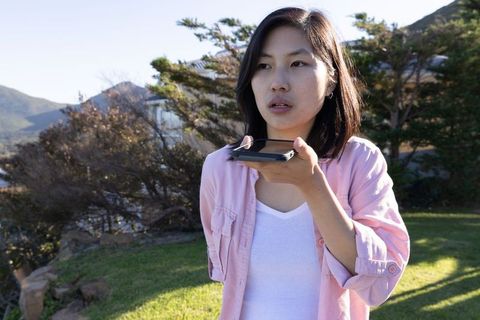 Asian Woman Communicating with Smartphone on Lawn Amid Nature