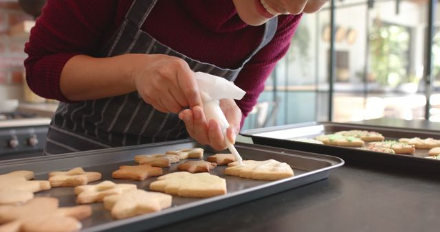 A person decorating homemade holiday cookies in a modern kitchen. This can be used for holiday-themed culinary content, cooking blogs, food magazines, social media posts on baking, and advertising baking products.