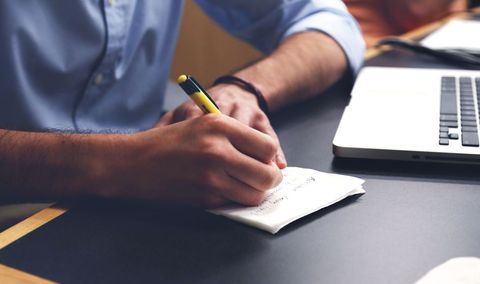 Person Taking Notes Beside Laptop in Study Environment