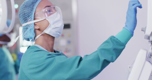 A healthcare professional in personal protective equipment (PPE) is operating advanced medical equipment within a hospital environment. This image portrays the dedication and precision of medical staff and is suitable for themes related to healthcare, medical technology, hospital care, safety protocols, and professional expertise.