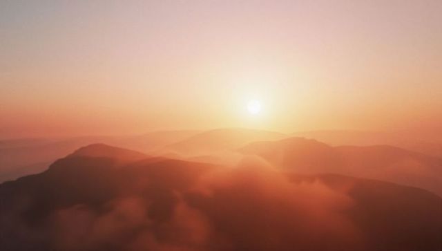 Serene sunrise over misty mountains with glowing sun