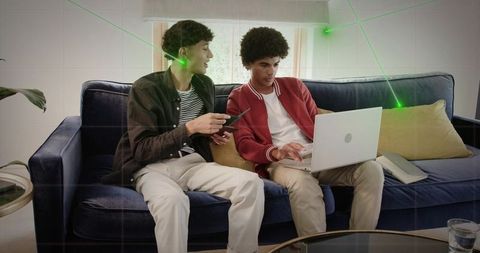 Young men collaborating on laptop and phone on couch with digital grid overlay for tech teamwork