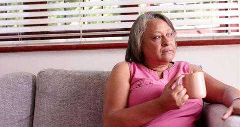 Senior woman sitting on couch drinking coffee lost in thought