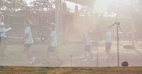 Children Playing Outdoors with Mentor Near Wind Turbines