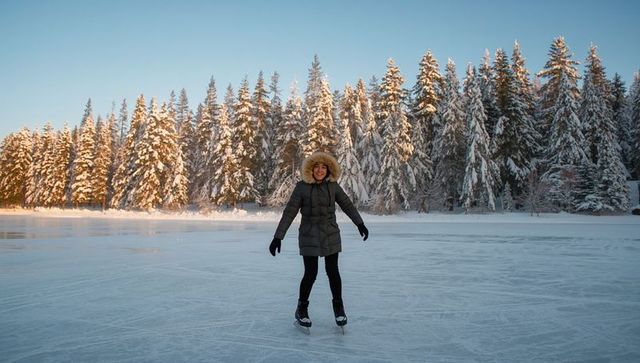 Woman skating on frozen lake at sunrise among snowy trees