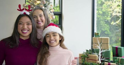 Smiling Multigenerational Family Celebrating Christmas by Window with Tree and Gifts