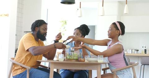 African american family sharing salad at bright modern kitchen dining table, bonding