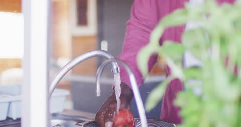 Elderly Man Washing Vegetables Under Kitchen Faucet in Rustic Setting