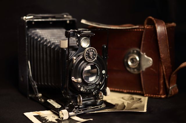 A beautifully preserved vintage bellows camera with a leather case resting nearby and two sepia-toned photographs, indicating an era gone by. Ideal for use in historical photography articles, nostalgic-themed collections, retro photography exhibits, and antique camera collections.