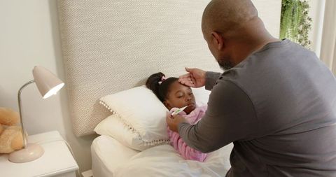 Caring father checking daughter's temperature in cozy bedroom
