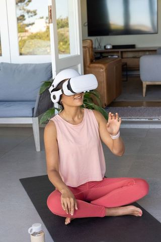 Woman practicing vr yoga on mat in living room with headset and water bottle