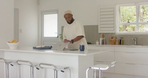African man working on laptop at minimalist kitchen island with coffee mug and smartphone