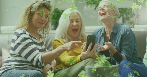 Three women laughing and sharing smartphone video on couch, friends enjoying moment