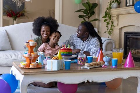 Joyful african american family celebrating child birthday with rainbow cake and balloons