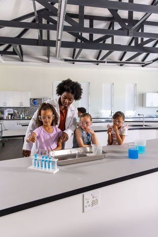 African american teacher guiding girls through hands-on science experiment in school lab