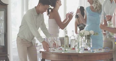 Friends Gathering Around Sunlit Table with Glassware, Wine Bottles and Floral Centerpiece