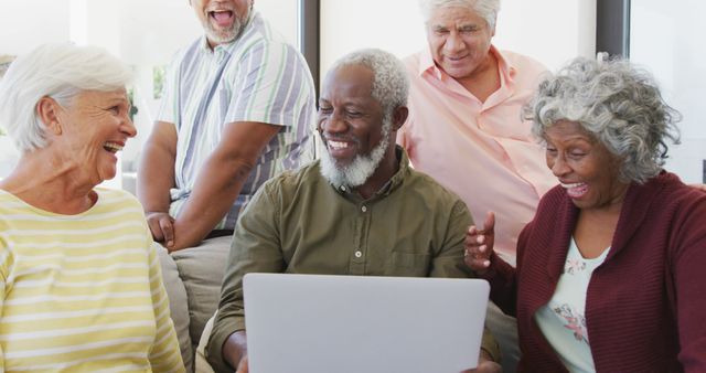 Senior friends are smiling and enjoying using a laptop together at home. Perfect for depicting senior lifestyle, technology use among older adults, and social connections among diverse friends.