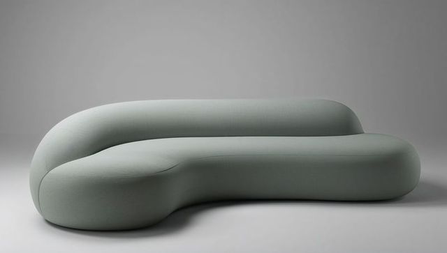 Sculptural curved sofa in pale sage woven fabric with seam detailing for minimal interiors