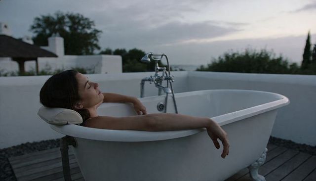 Reclining woman relaxing in white clawfoot bathtub on rooftop deck at twilight