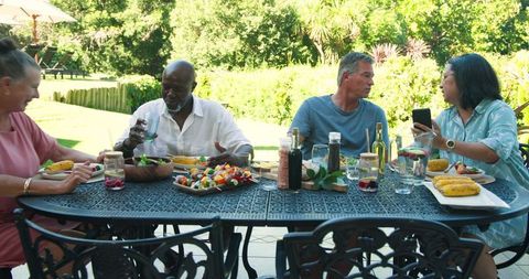 Diverse Friends Enjoying Outdoor Meal on Patio Under Lush Garden