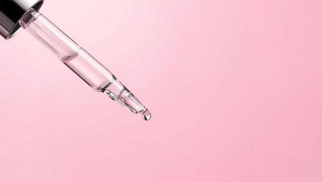 Glass dropper pipette with clear liquid on pink background
